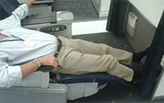 Zdjęcie mężczyzny siedzącego w Klasie Biznesowej, lekko leżącego, z wyciągniętymi nogami i bosymi stopami. 