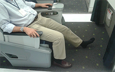Zdjęcie mężczyzny siedzącego w Klasie Biznesowej z wyciągniętą lewą nogą i bosą stopą.