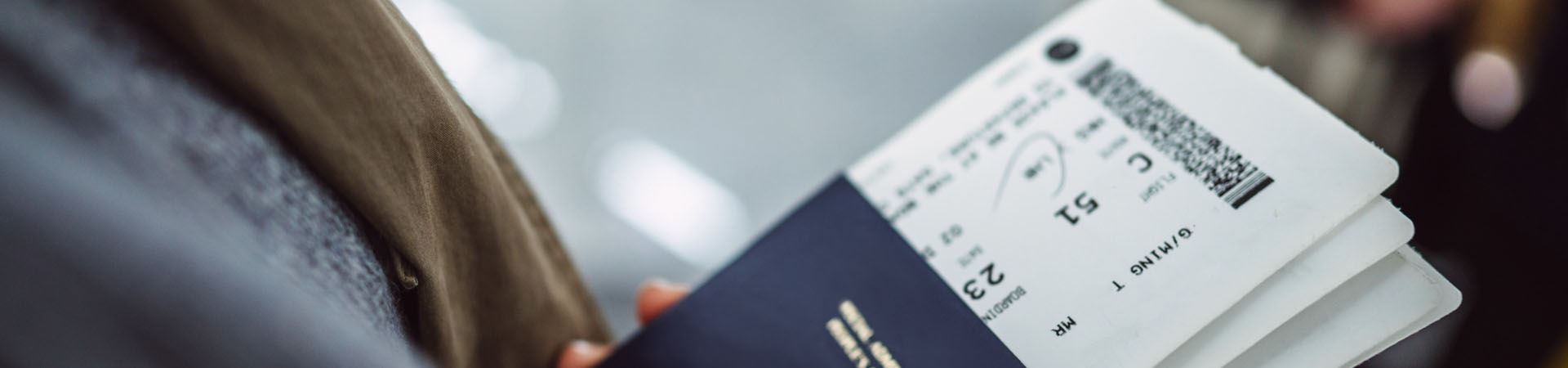 Fotografía de primer plano de una mano que sostiene tres pasaportes azul oscuro. Dentro de cada pasaporte hay una tarjeta de embarque.