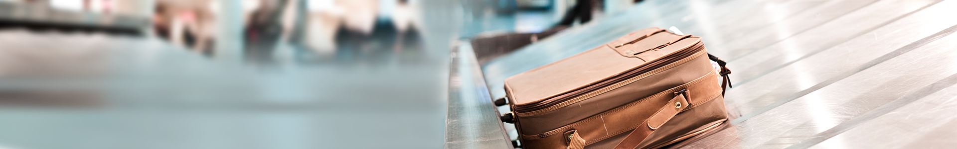 The image shows a brown suitcase lying on an airport luggage conveyor belt. Next to it there are no other suitcases. 