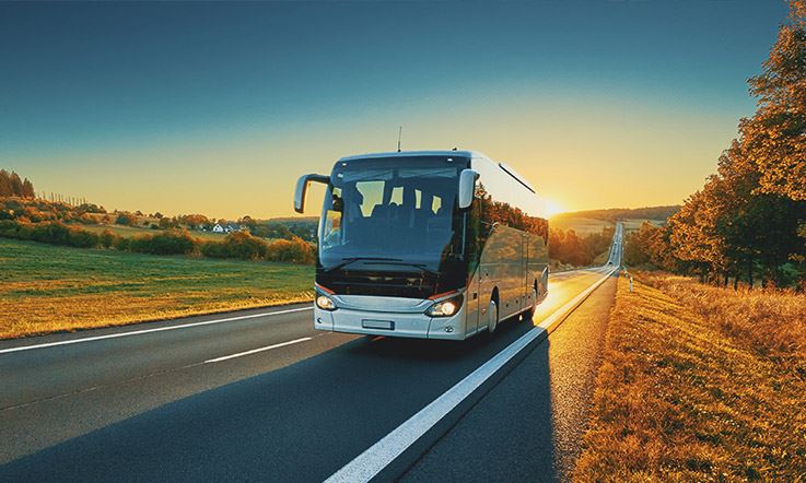 Zdjęcie białego autobusu na drodze pośrodku zielonego krajobrazu o zachodzie słońca. 