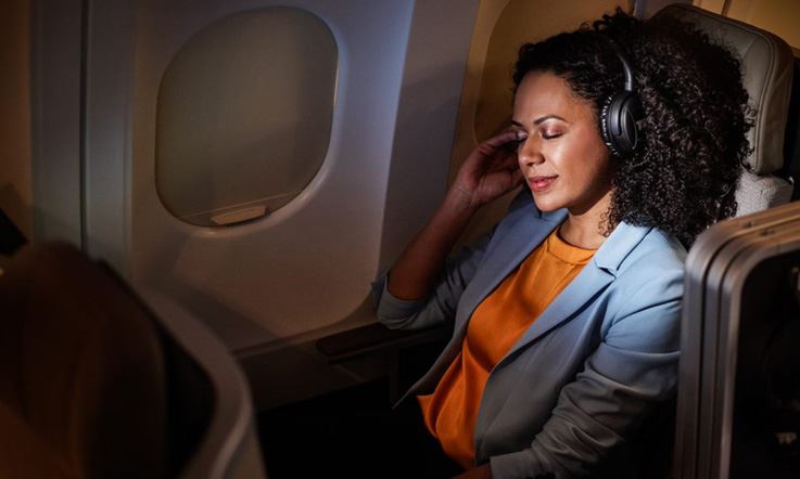 Passenger reclining in a comfortable and spacious Executive Class chair, in a calm and dark environment, with nobody around her. She is relaxed with her eyes closed, listening to music with the TAP headphones put on.