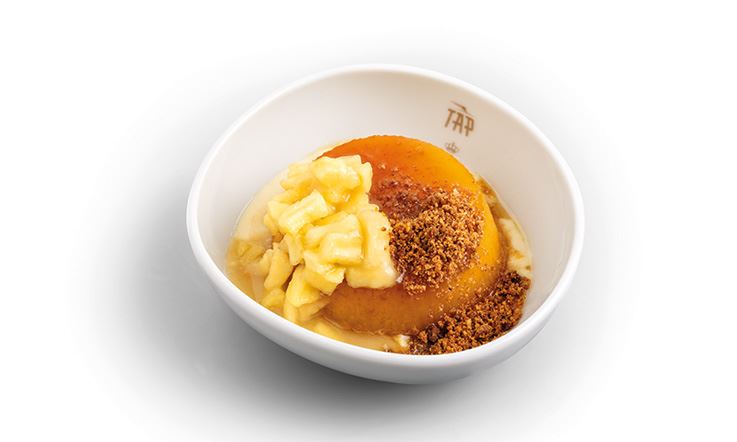 Zdjęcie białego talerza z logo TAP i deserem w postaci puddingu jabłkowego z kremem cynamonowo-migdałowym.