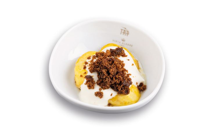 Foto de um prato branco com o logotipo da TAP e uma sobremesa composta por uma banana, cream cheese e bolo de mel de engenho.