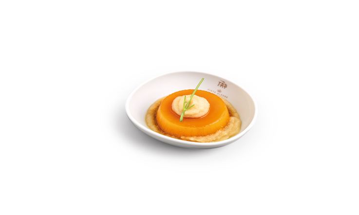 Fotografia de um prato branco com o logotipo dourado da TAP na borda. No prato, há pudim de amêndoas e mel Montesinho.