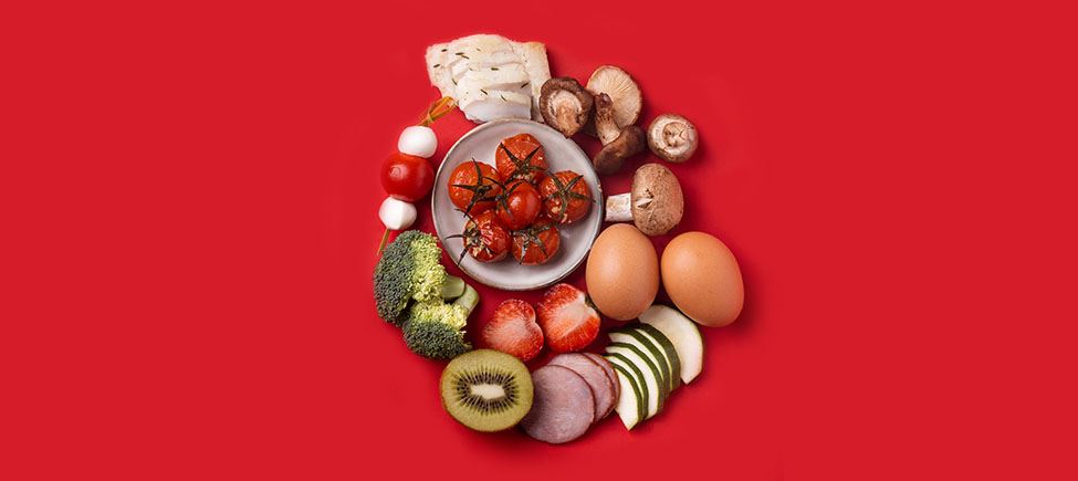 Фотография с различными продуктами, представляющими безглютеновую диету, на красном фоне: грибы, помидоры, брокколи, клубника, киви, яйца, огурец и другие продукты, подходящие для этого типа питания.