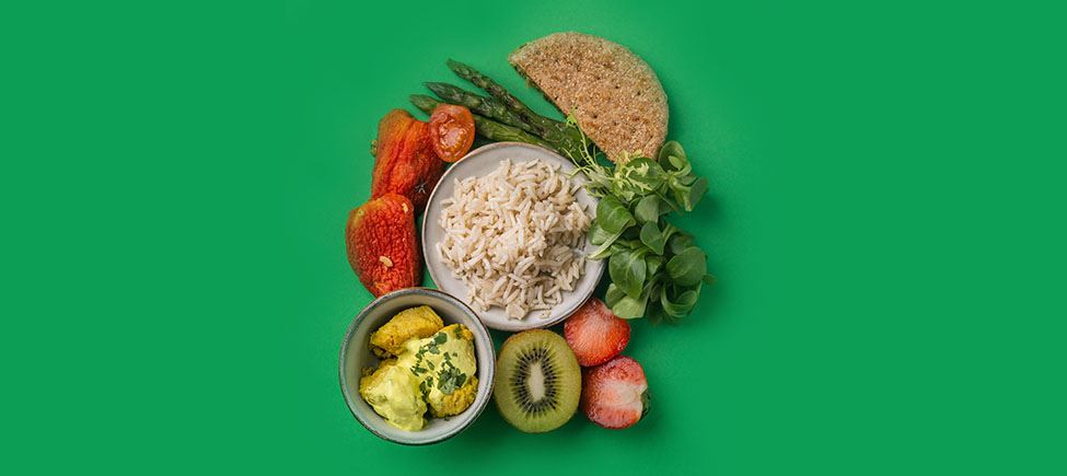 Фотография с различными халяльными продуктами, представляющими мусульманскую еду, на зеленом фоне: помидоры, клубника, спаржа, киви и другие продукты, подходящие для этого типа питания.